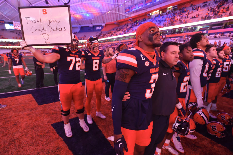 Syracuse interim head coach Nunzio Campanile, second from front left, stands with defensive back Isaiah Johnson, front left, as offensive lineman Mark Petry (72) holds a sign for former coach Dino Babers after their win over Wake Forest in an NCAA college football game in Syracuse, N.Y., Saturday, Nov. 25, 2023. Campanile took over for Babers who was fired earlier in the week. (AP Photo/Adrian Kraus)