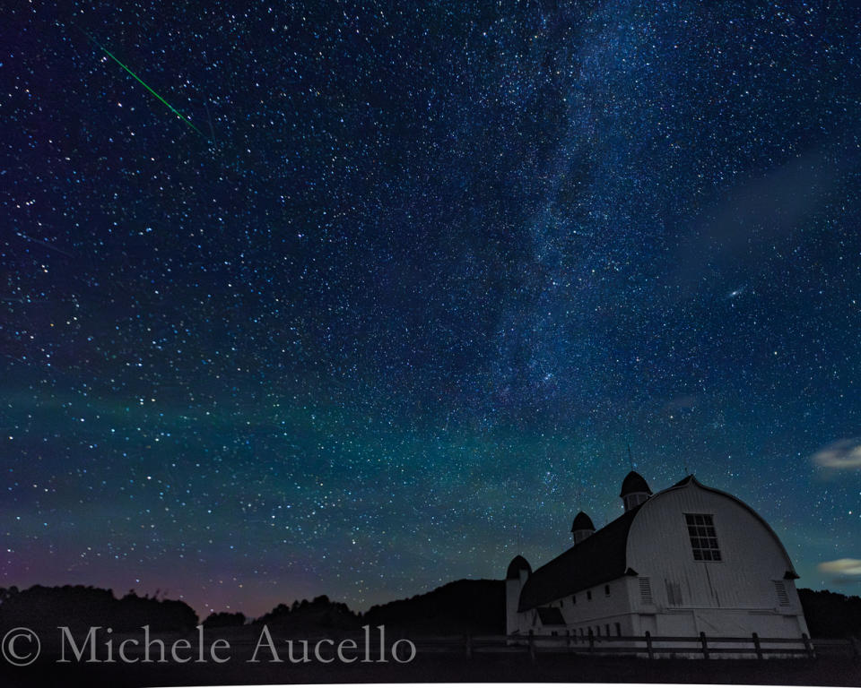 A meteor shower is pictured against a starry sky and picturesque foreground