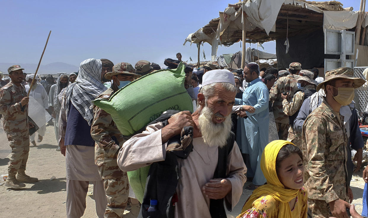 Pakistani soldiers stand guard while stranded people walk towards the Afghan side at a border crossing point, in Chaman, Pakistan, Friday, Aug. 13, 2021. Pakistan opened its Chaman border crossing for people who had been stranded in recent weeks. Juma Khan, the Pakistan border town's deputy commissioner, said the crossing was reopened following talks with the Taliban. (AP Photo/Jafar Khan)