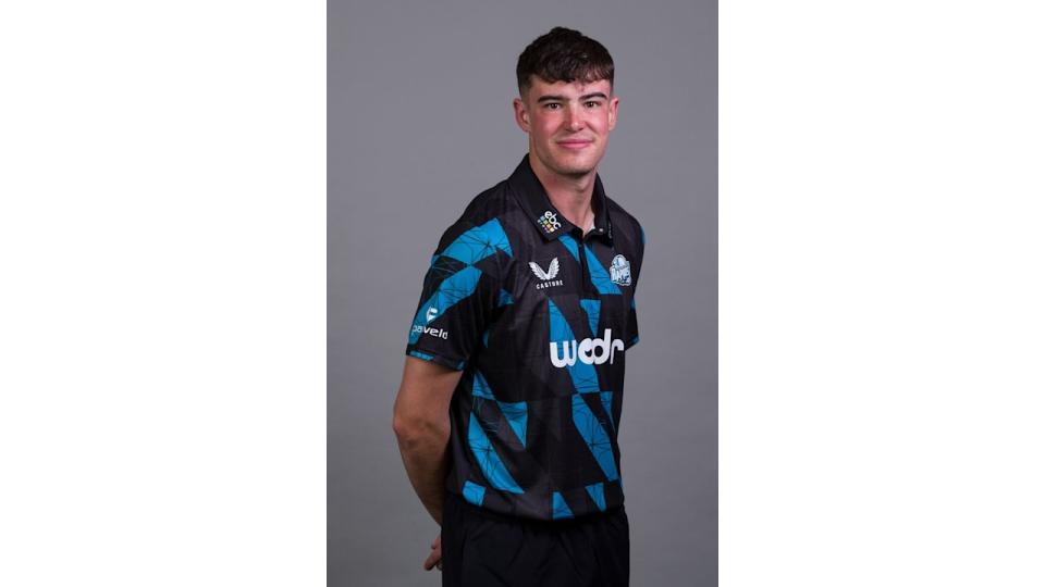 Jish Baker in a black and blue uniform in front of a grey background