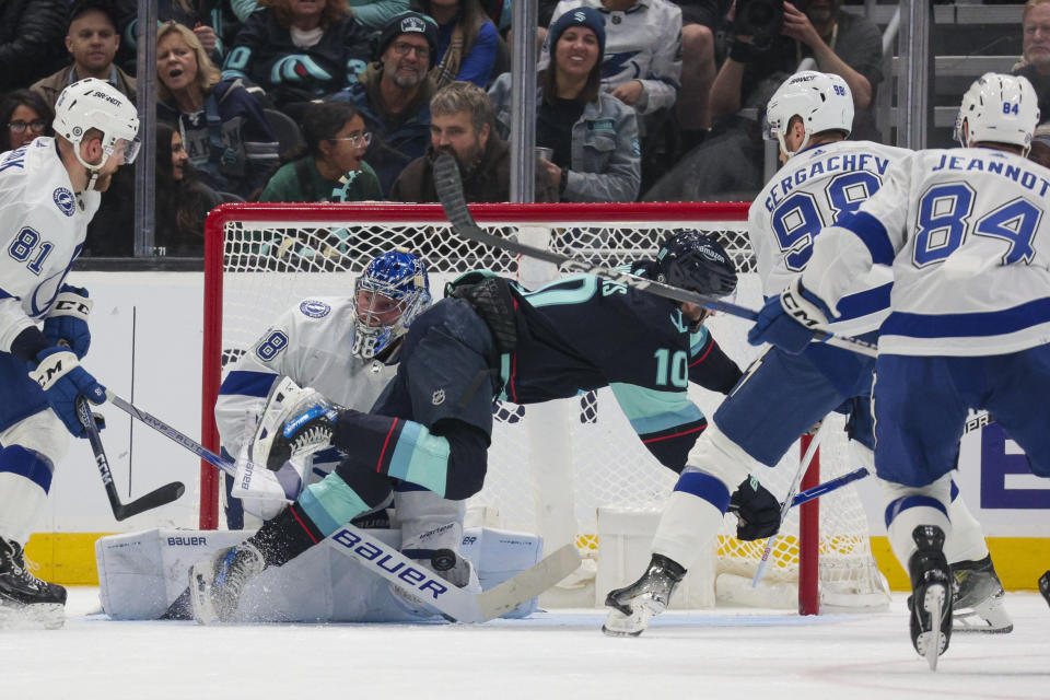 Seattle Kraken center Matty Beniers (10) goes down in front of the net as Tampa Bay Lightning goaltender Andrei Vasilevskiy (88) makes a save during the second period of an NHL hockey game Saturday, Dec. 9, 2023, in Seattle. (AP Photo/Jason Redmond)