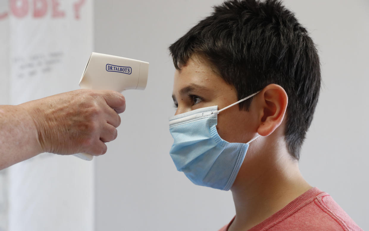 Amid concerns of the spread of COVID-19, sixth-grader Salih Tas wears a mask as he has his temperature checked by a teacher during a STEM summer camp at Wylie High School Tuesday, July 14, 2020, in Wylie, Texas. (AP Photo/LM Otero)