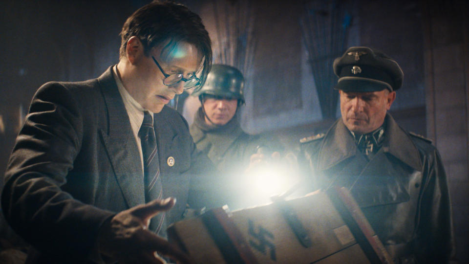 Mads Mikkelsen and Thomas Kretschmann looking into a glowing crate in Indiana Jones and the Dial of Destiny.