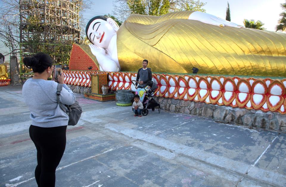 A family takes a picture in front of a giant statue of a reclining Buddha during the Cambodian New Year celebration at the Wat Dhammararam Buddhist temple in Stockton on Friday, Apr. 14, 2023. Thousands are expected to attend the 4-day cultural event which concludes on Sunday.