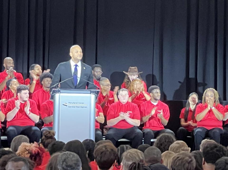 Maryland Gov. Wes Moore stands at the lectern during a launch event for the Service Year Option program at the University of Maryland, College Park on Oct. 27, 2023. Members of the Service Year Option and Maryland Corps programs are assembled behind and in front of him.
