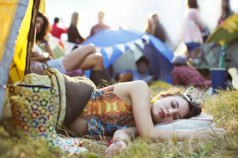 Woman with tiara sleeping in sleeping bag outside tents at music festival - stock photo