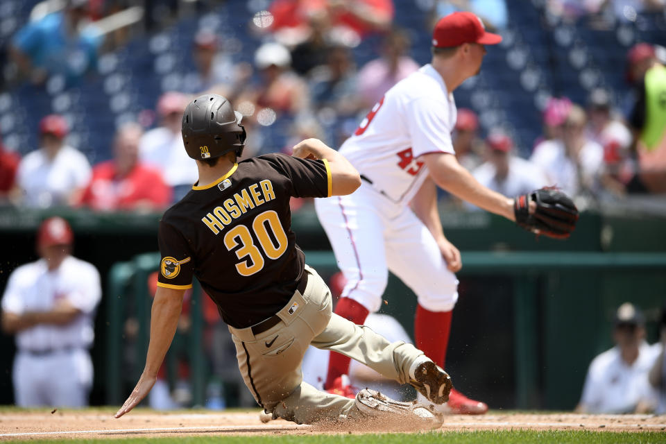 Eric Hosmer (30), de los Padres de San Diego, se barre en el plato para anotar con un sencillo de Tommy Pham al tiempo que el relevista Sam Clay, derecha, de los Nacionales de Washington, espera la pelota en el séptimo inning de la continuación de un partido un día antes, el domingo 18 de julio de 2021, en Washington. (AP Foto/Nick Wass)