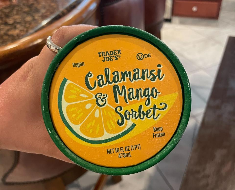 Hand holding a Trader Joe's Calamansi & Mango Sorbet tub in a kitchen