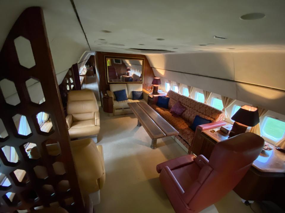 The lounge with couches, chairs, a mirror, and a table inside the plane.