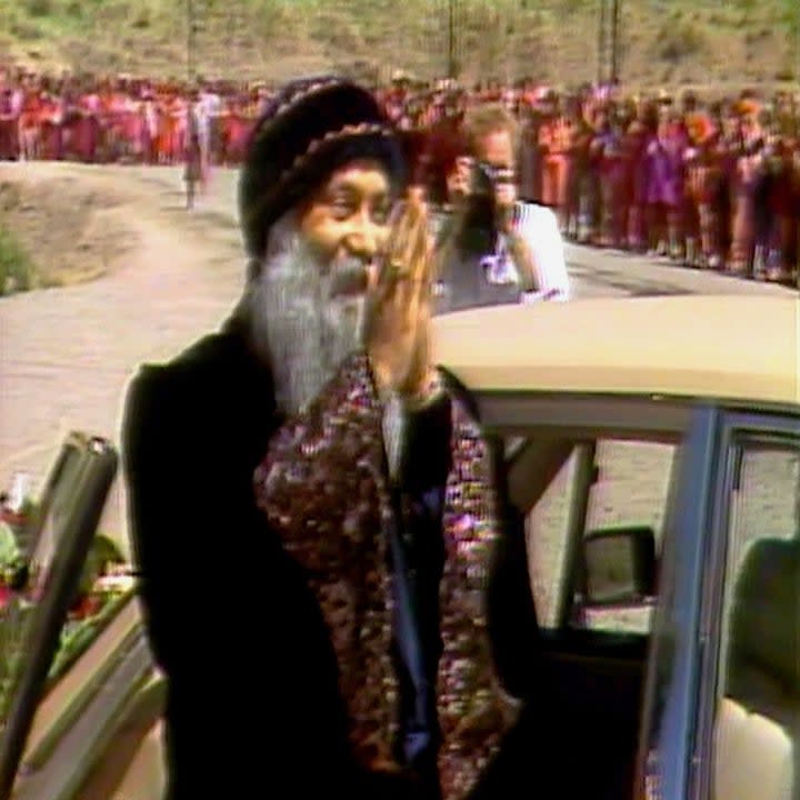 old man with prayer hands to a crowd watching as he stands by a car