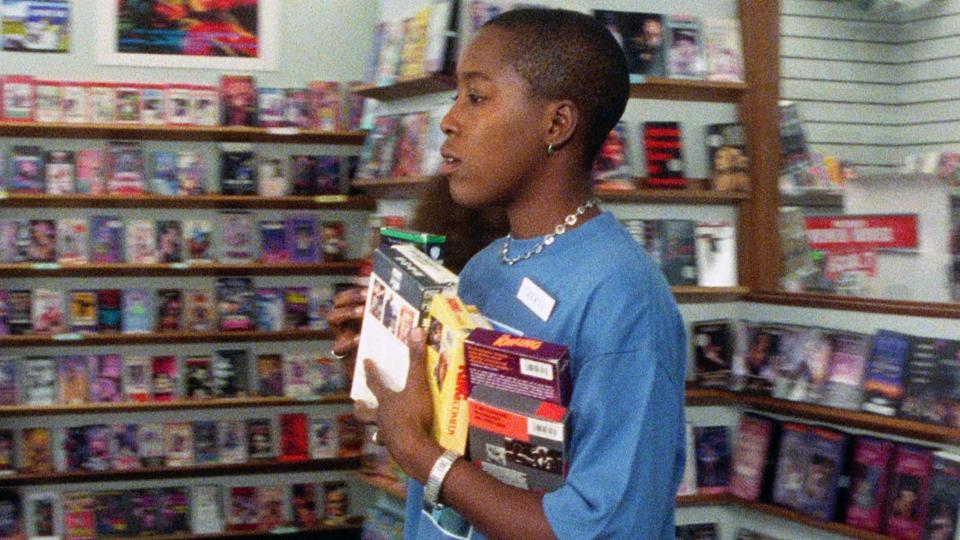 Person holding VHS tapes in a video rental store, which has shelves filled with various movie titles