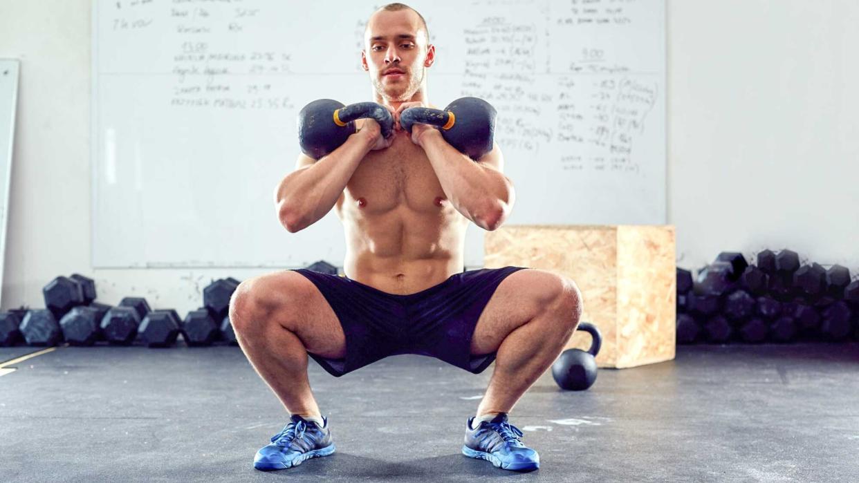  Man performing a kettlebell thruster with two kettlebells in squat position. 