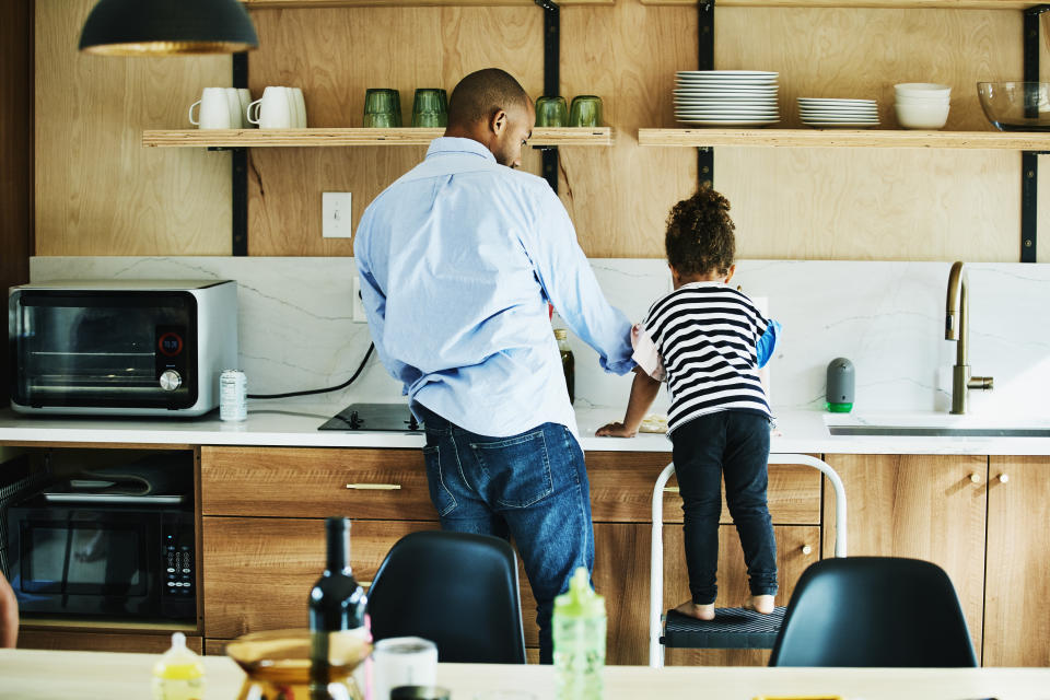 Young girl standing on stool in kitchen while helping father make dinner