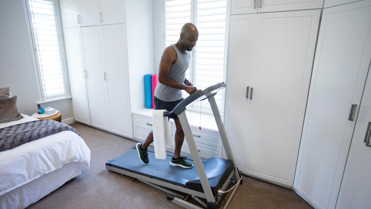 Mid section of man using smart watch while exercising on treadmill at home.