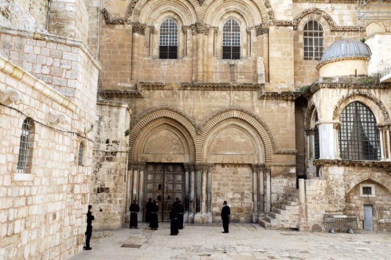 Roman Catholic monks pray in front of the locked door of Jerusalem's Church of the Holy Sepulchre amid coronavirus restrictions in the walled Old City