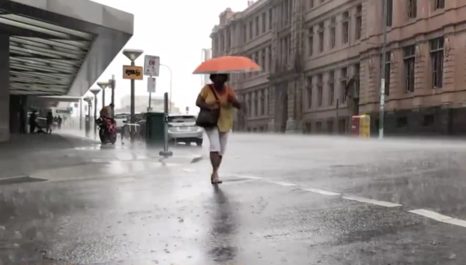 A woman walks through Brisbane's rain with an umbrella.