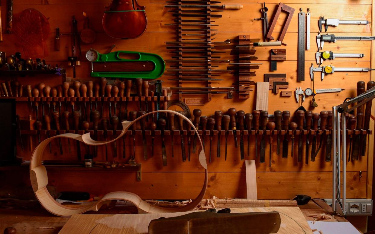 A wooden shell, to be made into a violin, is seen in a luthier's workshop where large numbers of woodworking tools hang from the wall - Miguel Medina/AFP via Getty Images