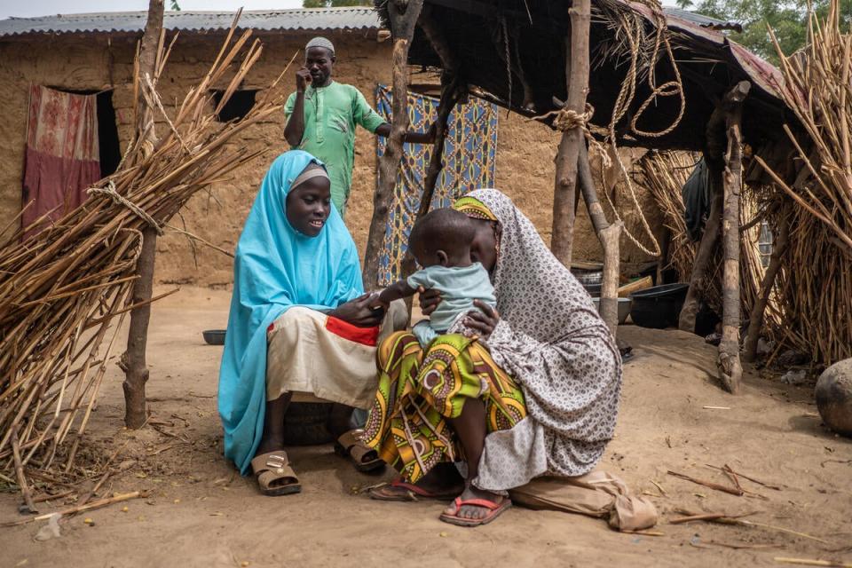 Mallam looks on as Aisha, 30, and Hauwa, 15, play with Bashir, one, outside their home (Yagazie Emnezi/Save The Children)