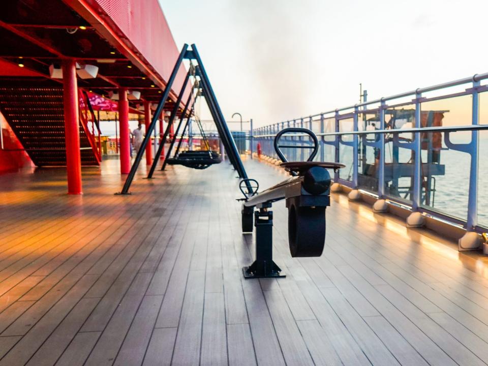 An empty deck on a cruise ship with a black seesaw, swings, and  a red staircase