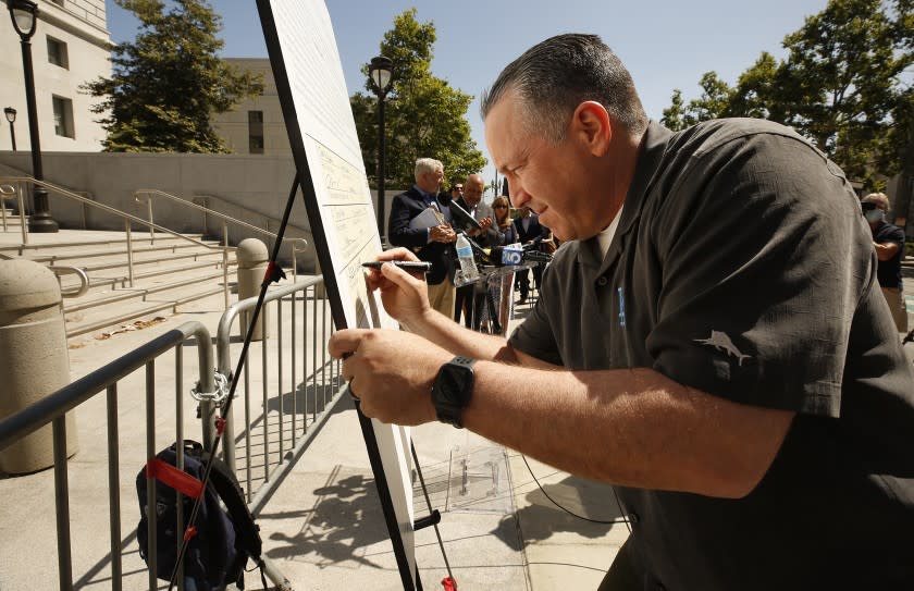 LOS ANGELES, CA - MAY 26: LA County Sheriff Alex Villanueva signs a large version of the petition to recall L.A. County D.A. George Gascon at a press conference on Wednesday morning in front of the Hall of Justice in downtown LA. Desiree Andrade, whose son Julien Andrade was murdered in 2018 and Tania Owen, widow of Los Angeles County Sheriff's Department Sgt. Steve Owen murdered in 2016, co-organizers of the recall, kicked off the effort. LA County Sheriff Alex Villanueva, former LA County District Attorney Steve Cooley and former LA City Councilman Dennis Zine were there in support. Hall of Justice on Wednesday, May 26, 2021 in Los Angeles, CA. (Al Seib / Los Angeles Times).