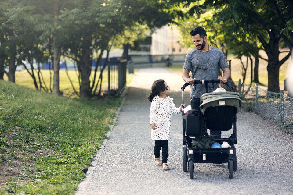 Father and daughter talking while walking with baby stroller on footpath at park