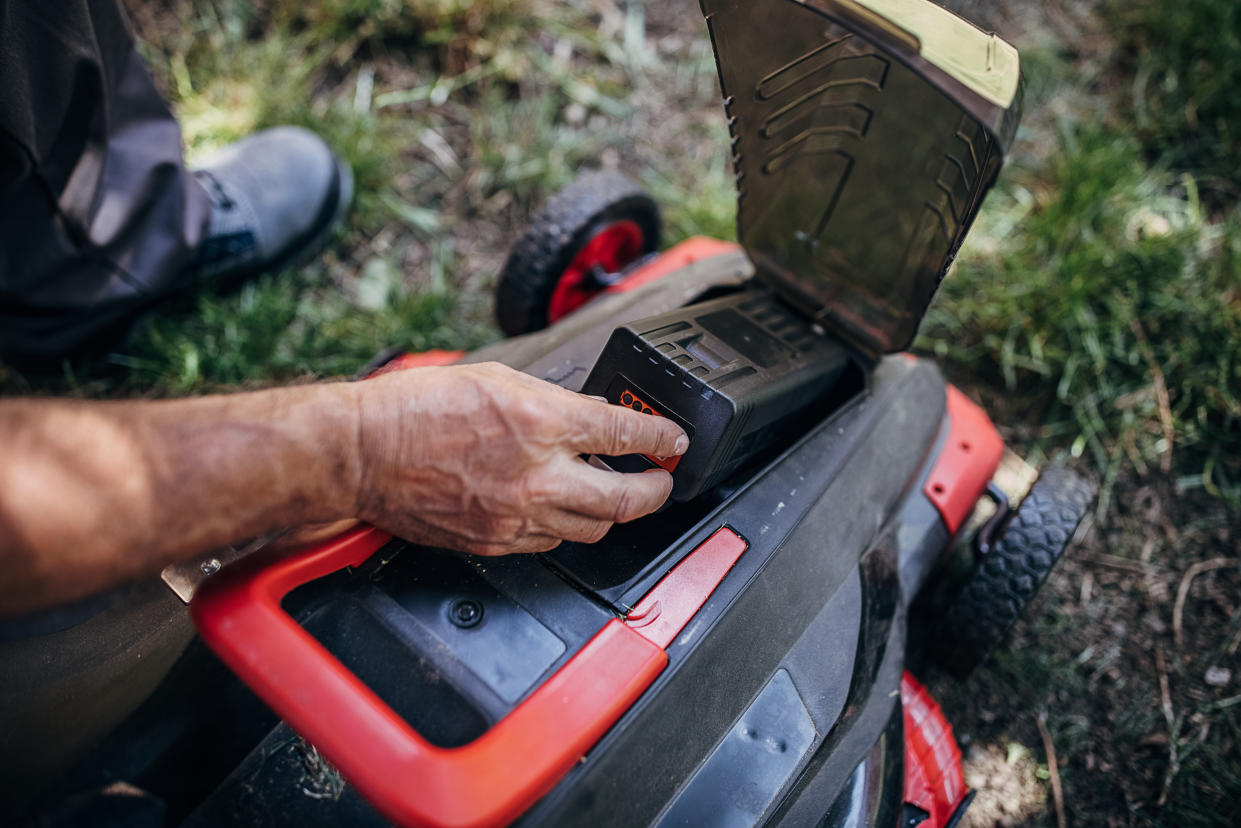 A man testing the battery in electric cordless lawn mower. 