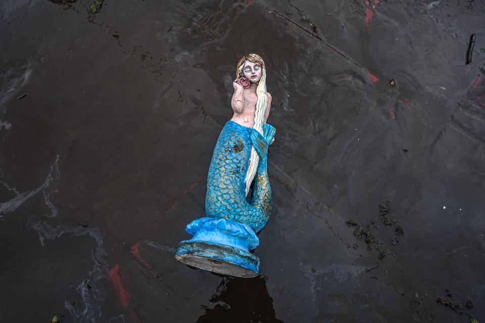A statue of a mermaid with blond hair and a blue tail is washed up on the shore.