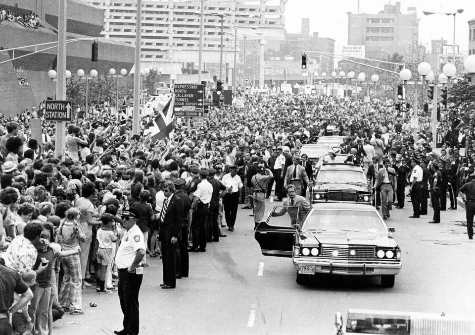 Queen Elizabeth II and Boston mayor Kevin White (in second car) ride along Congress Street, waving to the crowd outside City Hall during her visit to Boston, July 11, 1976.