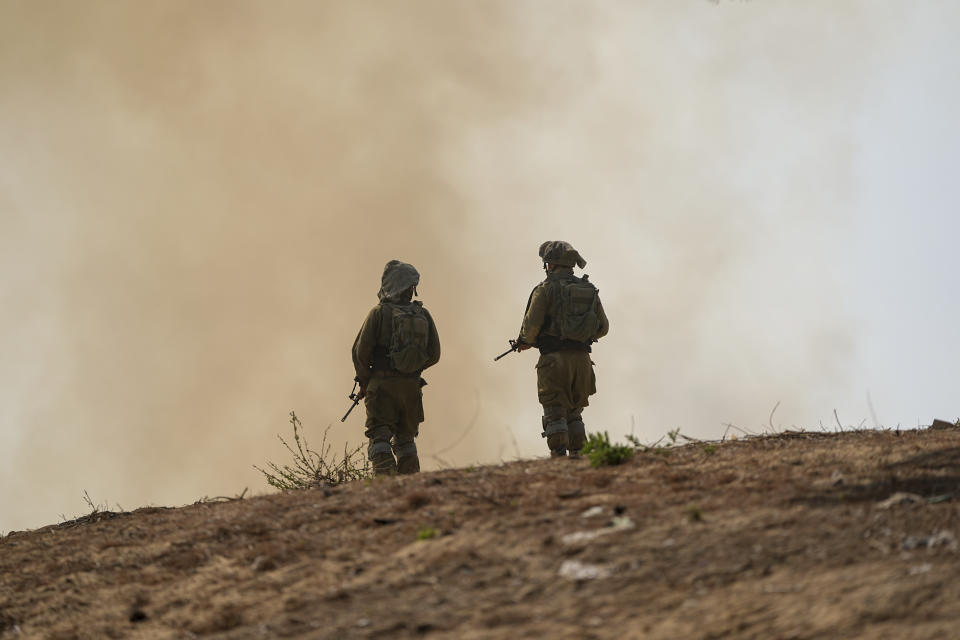 Israeli soldiers stand next to a burning field near the border with the Gaza Strip, in southern Israel, Tuesday, Oct. 24, 2023. (AP Photo/Ohad Zwigenberg)
