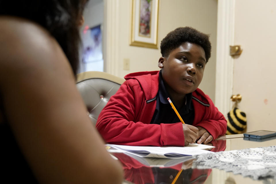 Evena Joseph, left, sits with her son J. Ryan Mathurin, 9, as he does his homework, Thursday, Dec. 22, 2022, at their home, in Boston. (AP Photo/Steven Senne)