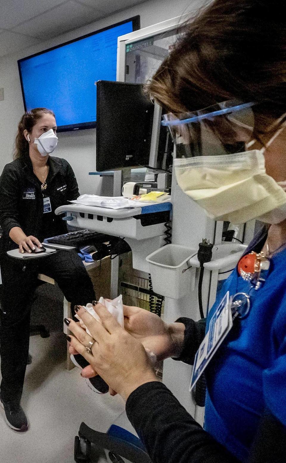 Nurse Alix Zacharski, right, sanitizes her hands as other doctors and nurses care for a patient in the COVID unit at Jackson Memorial Hospital in July 2021. As the omicron variant leads to a record number of COVID cases in South Florida, hospitals are contending with staff shortages as employees contract COVID.