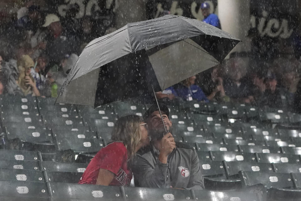 Fans sit under an umbrella during a rain delay in the third inning of a baseball game between the Los Angeles Dodgers and the Cleveland Guardians, Wednesday, Aug. 23, 2023, in Cleveland. (AP Photo/Sue Ogrocki)