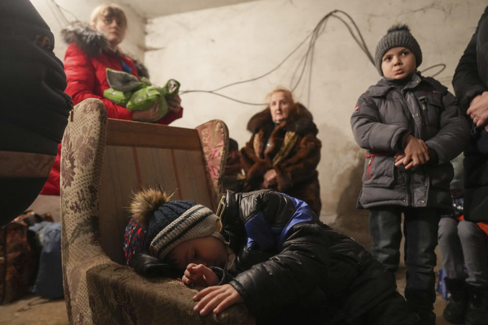 A child sleeps in an armchair as other stands around in a shelter during Russian shelling, in Mariupol, Ukraine. (Evgeniy Maloletka / AP)