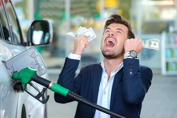 A screaming man with money in his hands while pumping gas.