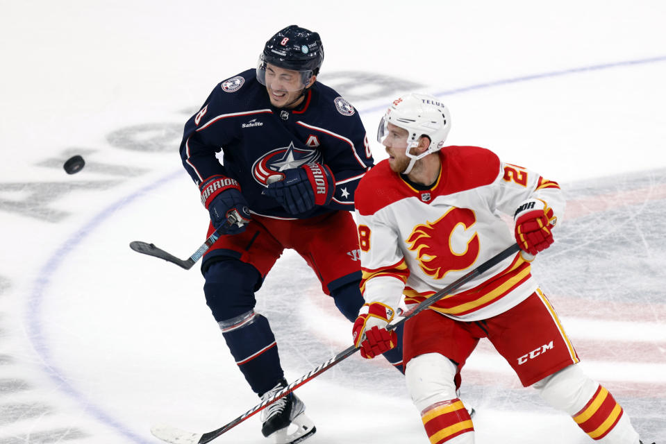 Columbus Blue Jackets defenseman Zach Werenski, left, and Calgary Flames forward Elias Lindholm chase the puck during the third period of an NHL hockey game in Columbus, Ohio, Friday, Oct. 20, 2023. (AP Photo/Paul Vernon)