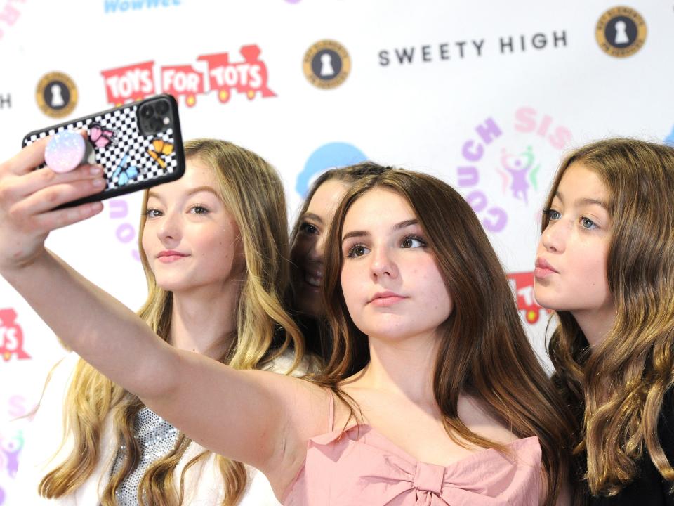 piper rockelle, center, holding her phone up at an angle to take a selfie of her and several other friends at a toys for tots event