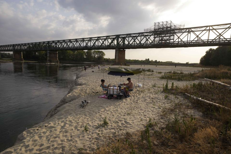 People relax at sunset on the Po riverbed next to Ponte della Becca (Becca Bridge) in Linarolo, near Pavia, Italy, Monday, June 27, 2022. Italy's largest river, which is turning into a long stretch of sand due to the lack of rain, is leaving the Lomellina rice flats — nestled between the river Po and the Alps — without the necessary water to flood the paddies. (AP Photo/Luca Bruno)
