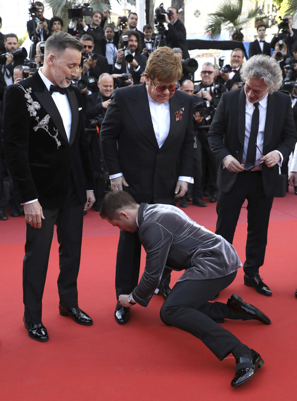 Actor Taron Egerton, center, ties the shoelaces of singer Elton John, center top, as they pose with producer David Furnish, director Dexter Fletcher, actor Richard Madden, producer Adam Bohling and music producer Giles Martin upon arrival at the premiere of the film 'Rocketman' at the 72nd international film festival, Cannes, southern France, Thursday, May 16, 2019. (Photo by Vianney Le Caer/Invision/AP)