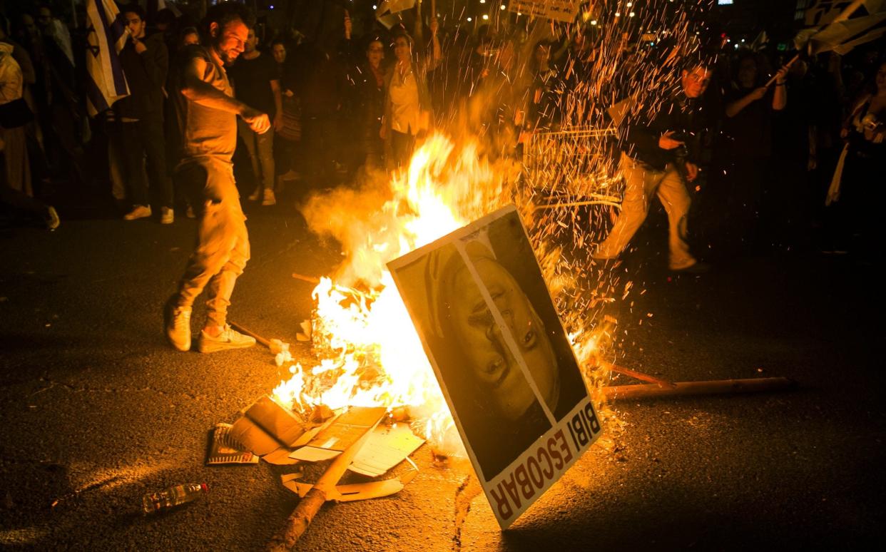 Protesters in Tel Aviv on Monday night burn a placard showing Benjamin Netanyahu