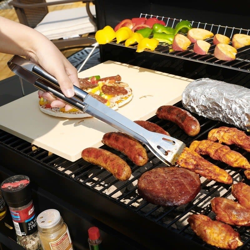 model using the silver tongs to flip meat on a grill