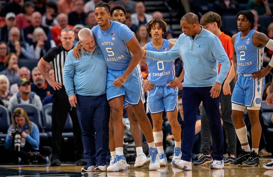 North Carolina trainer Doug Halverson and coach Hubert Davis help Armando Bacot (5) off the court after an injury in the opening minutes of play against Virginia on Tuesday, January 10, 2023 at John Paul Jones Arena in Charlottesville, Va.