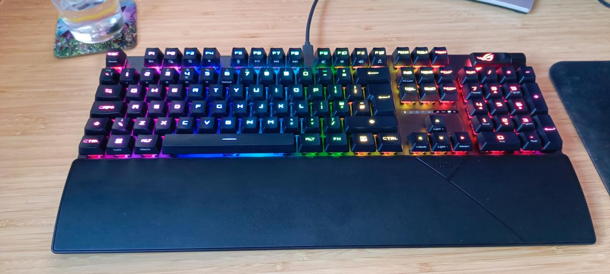  A black ASUS ROG Strix Scope II RX gaming keyboard on a wooden desk. 