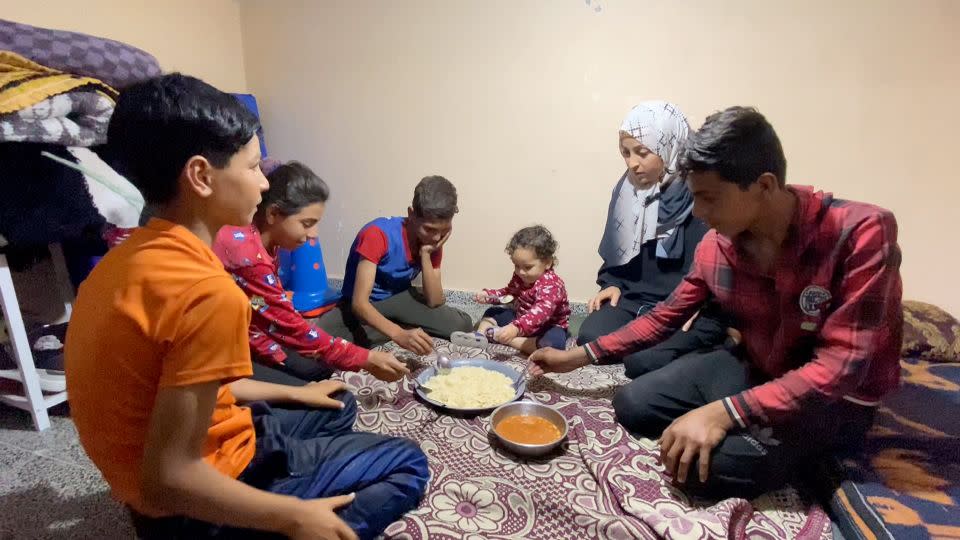 Um Hassan (second from right) is pictured eating food provided by World Central Kitchen on May 1, in Deir al-Balah, in central Gaza. The mother told CNN her toddler (center) is "happy to eat rice." - CNN