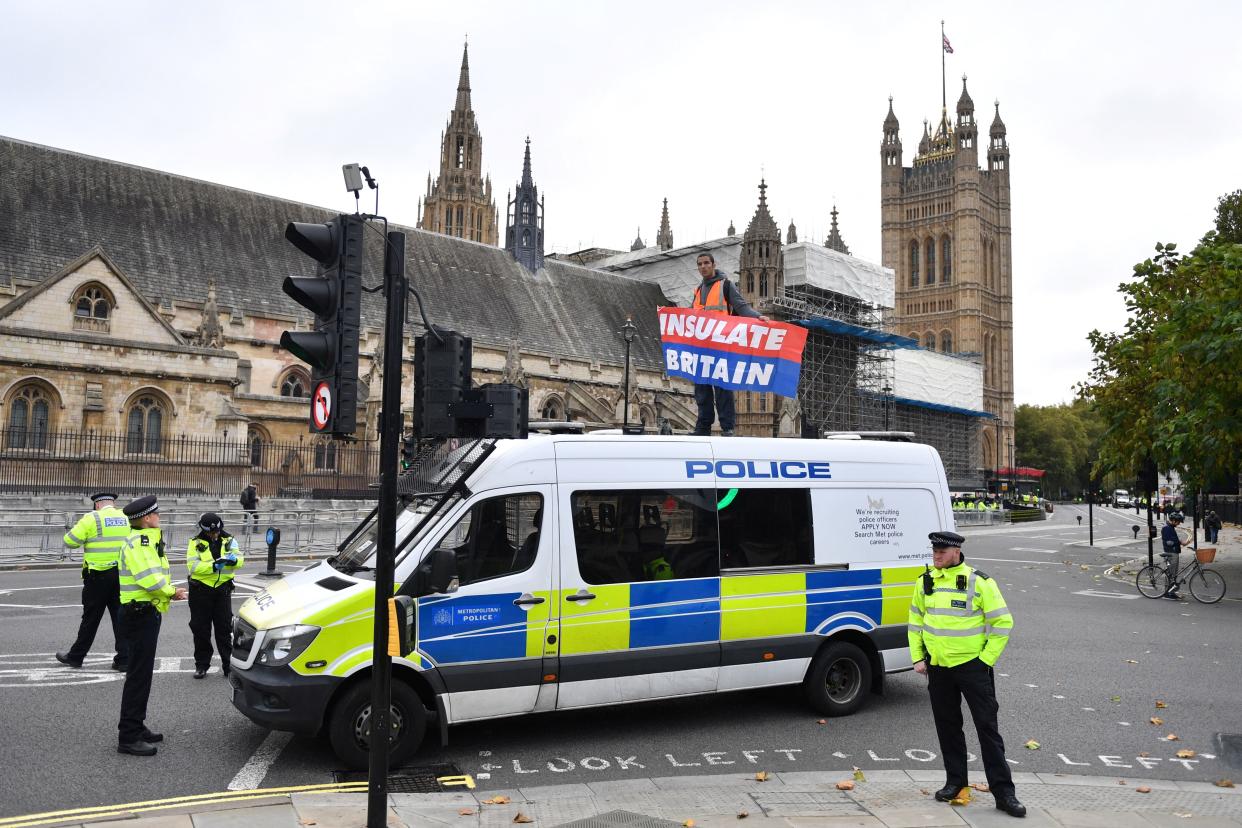 Police officers monitor an environmental activist from the group Insulate Britain waving a banner from atop a police van at Parliament Square in central London on November 4, 2021, as protestors call for the UK government to fund the insulation of Britain's homes. - Insulate Britain, a new group whose campaigners have repeatedly blocked roads and motorways in and around the capital, want the government to insulate all British homes starting with social housing. (Photo by JUSTIN TALLIS / AFP) (Photo by JUSTIN TALLIS/AFP via Getty Images)