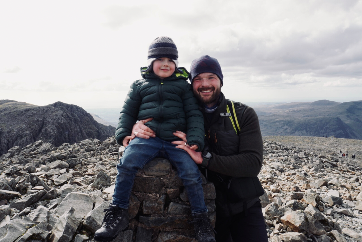 A boy sitting on a rock, with his dad holding him