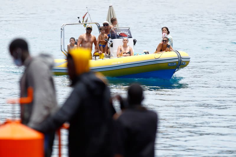 A group of tourists on a boat observes several migrants waiting to disembark from a Spanish coast guard vessel, in the port of Arguineguin