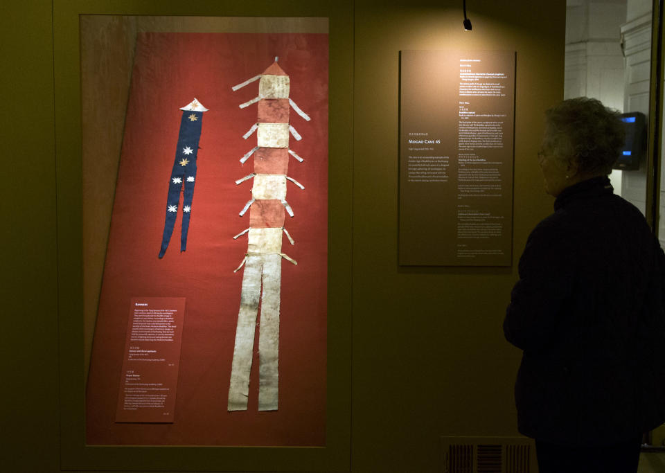 A woman looks at a silk banner with floral appliquets, left, and a preyer banner, displayed in "Dunhuang: Buddhist Art at the Gateway of the Silk Road," at the China Institute, in New York, Tuesday, April 24, 2013. (AP Photo/Richard Drew)