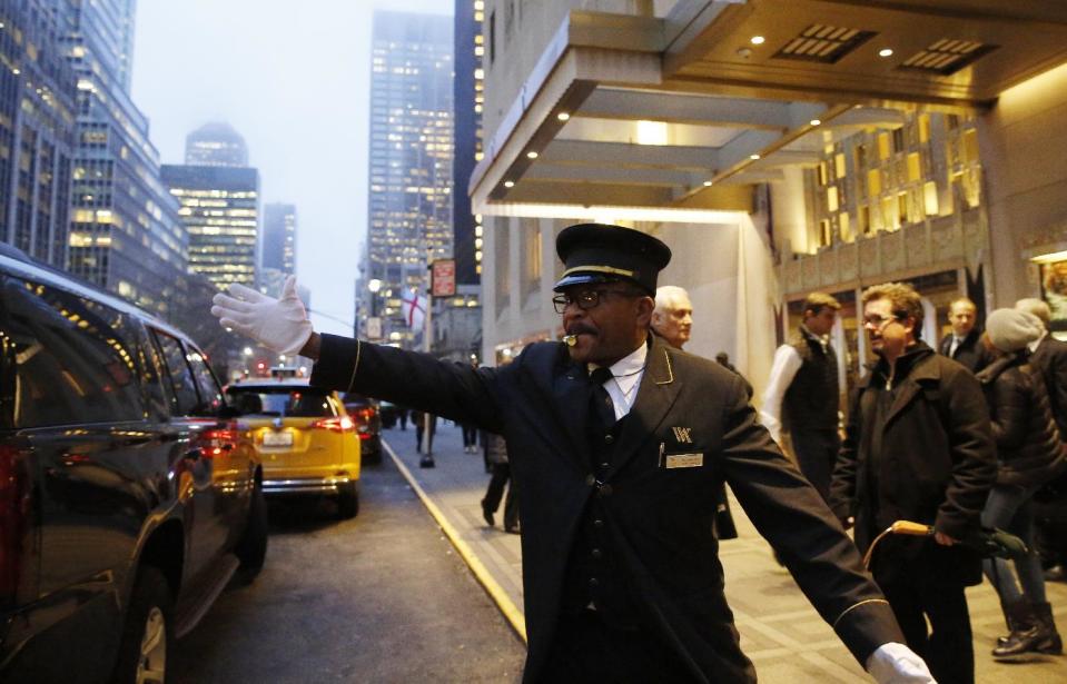 Veteran doorman Thales Cadet, who claims, "the world comes to me everyday," hails a cab in front of the Waldorf Astoria hotel, Tuesday, Feb. 28, 2017, in New York. Cadet has worked at the hotel for 12 years since coming from his former job at the Plaza Hotel. The hotel, purchased by the Anbang Insurance Group, a Chinese company, is closing Wednesday for two to three years for renovation. (AP Photo/Kathy Willens)