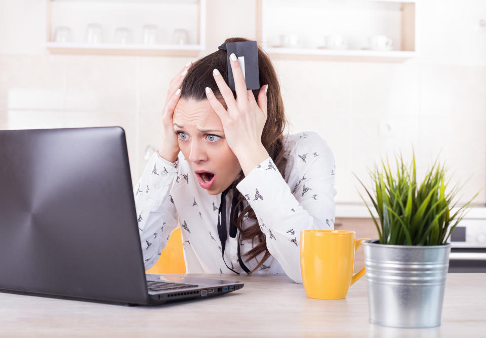 Shocked young woman holding credit card and looking at laptop. Negative surprise in e-banking