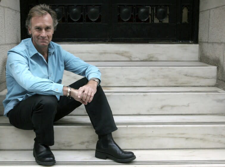 A man in a blue dress shirt and black pans sits on marble stairs